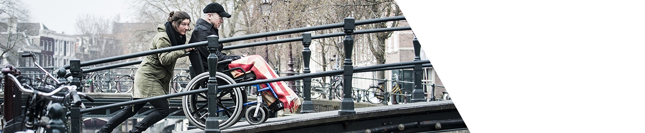 Persoon duwt iemand in een rolstoel een brug op in Amsterdam.